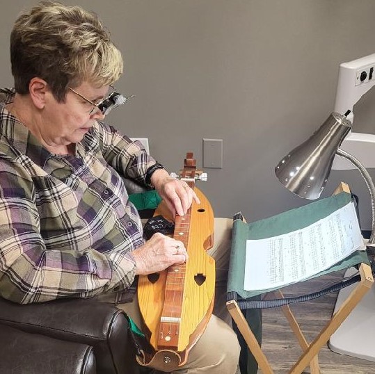Dr. Long's low vision patient using special telescopic glasses to play the dulcimer
